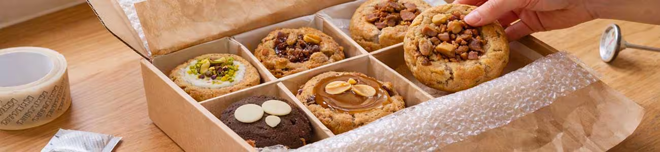 Préparation d'une commande de cookies Opaléia pour l'expédition Main plaçant un cookie artisanal dans une boîte d'expédition Opaléia